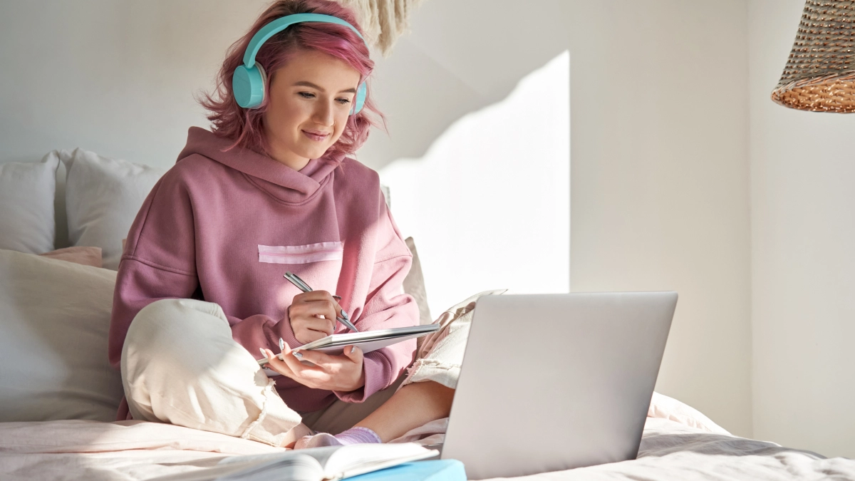 Vrouw met koptelefoon op bed achter laptop – Studentenpakket – Particulier