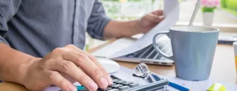 Man achter bureau op rekenmachine – Ziekengeldverzekering – Zakelijk