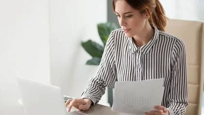 Vrouw op laptop met papieren – Ziekengeldverzekering – Zakelijk
