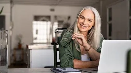 Vrouw zit aan tafel met laptop lacht – Pensioen – Zakelijk