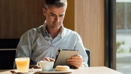 Man aan tafel met koffie en donut op I-pad – Hypotheek – Zakelijk