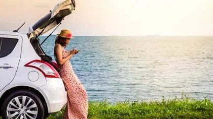 Vrouw staat tegen auto aan op mobiel aan het water – Coronavirus – Particulier
