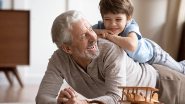 Happy,Little,Schoolboy,Lying,On,Older,Senior,Grandfather,On,Floor