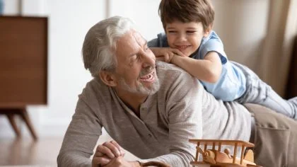 Happy,Little,Schoolboy,Lying,On,Older,Senior,Grandfather,On,Floor