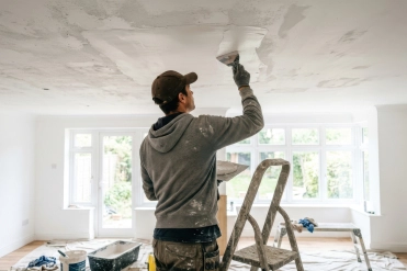 Professional plasterer skimming and smoothing a ceiling in a home